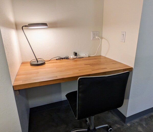 Una scrivania in legno con una sedia da ufficio nera, una lampada da tavolo e una presa di corrente.