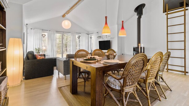 Un vaste espace de vie comprenant une table à manger, des chaises en osier et une cheminée.