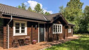 Une cabane en bois avec un toit en tuiles, une véranda avec un banc et une porte dotée d’une fenêtre.