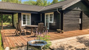 Une cabane en bois dotée d’un patio couvert, d’une table et de chaises, ainsi que d’un abreuvoir pour oiseaux.