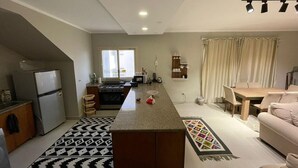 A compact kitchen with a central island, a dining area with a table and chairs, and a living space with a sofa. - Golfview House HaciendaBay Families Only (El Alamein)