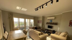 A modern living room with a dining table, sofas, and a TV. - Golfview House HaciendaBay Families Only (El Alamein)