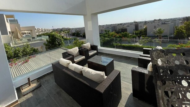 A rooftop terrace with outdoor furniture, a glass balustrade, and a view of the cityscape. - Golfview House HaciendaBay Families Only (El Alamein)
