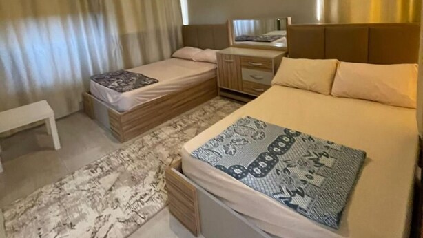 Ein Hotelzimmer mit zwei Betten, einem kleinen Schreibtisch, einer Bank und einem gemusterten Teppich.