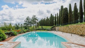 A swimming pool with a stone wall and a grassy area with trees. - Casale Ginestra by MMega (San Gimignano)