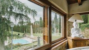 A room with a large window overlooking a pool and garden, a statue, and a lamp. - Casale Ginestra by MMega (San Gimignano)