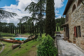 A stone building with a pool, surrounded by trees and a garden.