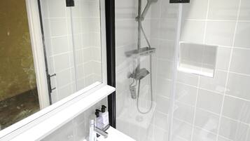 A modern bathroom with a glass-enclosed shower, a white sink, and a mirror.
