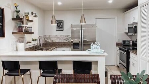 A modern kitchen with a central island, two pendant lights, and a refrigerator. - Family Fun, Pool,Theater, Backyard, Early Check-in (Palm Bay)