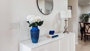 A white console table with a blue vase of white flowers, a book, and a mirror on the wall. - Family Fun, Pool,Theater, Backyard, Early Check-in (Palm Bay)