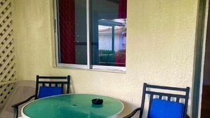 Eine Terrasse mit rundem Tisch und zwei Stühlen, ein Fenster mit Ausblick und ein Gitterwerk.