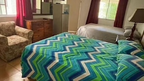 Ein Hotelzimmer mit Bett, Sessel, Schreibtisch, Fernseher und Deckenventilator.