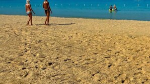 Ein Sandstrand mit Fußspuren, ein klarer, blauer Himmel und ein Schiff in der Ferne.