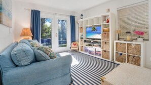 Una sala de estar con un sofá azul, un televisor y un mueble blanco para entretenimiento.