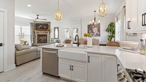 A modern kitchen with white cabinetry, a central island, pendant lighting, and a fireplace.