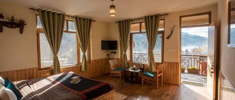 A cozy room with a bed, a small table, chairs, a TV, and large windows offering a mountain view.