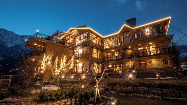 Un hôtel à plusieurs étages doté d’un balcon et d’un espace extérieur aménagé, entouré de montagnes.