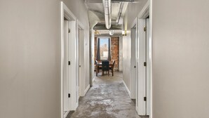 A hallway with white walls, a brick wall at the end, and a table with chairs. - The Nelson Lofts - Unit 7 (2 BR) (Davenport)