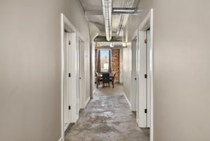 A hallway with white walls, a brick wall at the end, and a table with chairs. - The Nelson Lofts - Unit 7 (2 BR) (Davenport)