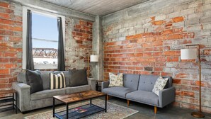 A room with two grey sofas, a wooden coffee table, a patterned rug, and a brick wall. - The Nelson Lofts - Unit 7 (2 BR) (Davenport)