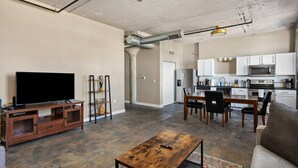 A living room with a TV, wooden coffee table, and a dining area with chairs and a table. - The Nelson Lofts - Unit 7 (2 BR) (Davenport)