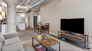 A modern living room with a TV, wooden coffee table, and a dining area with chairs. - The Nelson Lofts - Unit 4 (2 BR) (Davenport)