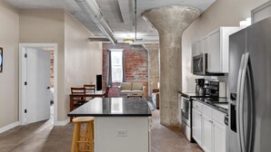 A modern kitchen with a central island, stainless steel appliances, and a brick wall in the background. - The Nelson Lofts - Unit 4 (2 BR) (Davenport)