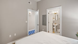 A bedroom with a large bed, a bathroom with a sink and mirror, and a door leading to another room. - The Nelson Lofts - Unit 6 (1 BR) (Davenport)