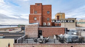 A multi-story brick building with a rooftop patio area featuring outdoor seating. - The Nelson Lofts - Unit 6 (1 BR) (Davenport)