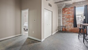 Un espacio abierto con techo de hormigón visto, pared de ladrillo decorativa y una puerta que da a un dormitorio.