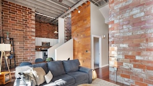 A modern living room with a grey sofa, wooden coffee table, and a brick wall. - The Nelson Lofts Penthouse (2BR) (Davenport)