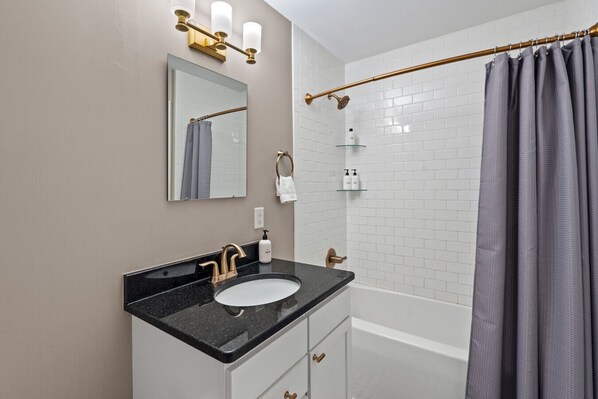 Une salle de bain avec un lavabo à vasque et un plan de toilette noir, un miroir, un porte-serviettes et un rideau de douche.