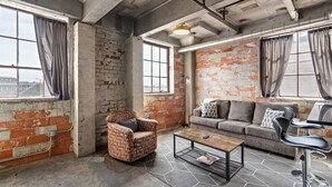 Une pièce avec des murs en briques apparentes, un canapé, un fauteuil, une table basse et de grandes fenêtres.