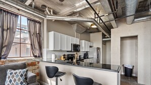Une cuisine moderne avec des meubles blancs, des appareils en acier inoxydable et un coin bar doté de tabourets noirs.