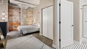 A bedroom with a bed, a wardrobe, a ceiling fan, a brick wall, and a door. - The Nelson Lofts - Unit 3 (2 BR) (Davenport)