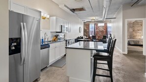 A modern kitchen with stainless steel appliances, white cabinetry, and a central island with bar stools. - The Nelson Lofts - Unit 3 (2 BR) (Davenport)