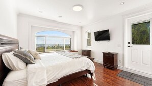 Une chambre avec un grand lit, un téléviseur fixé au mur et une fenêtre donnant sur un beau paysage.