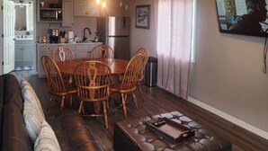 A living room with a brown leather sofa, a wooden dining table with chairs, a ceiling fan, and a kitchen area with appliances. - 3 bedroom 1 bath above garage guest house (Shoshone)