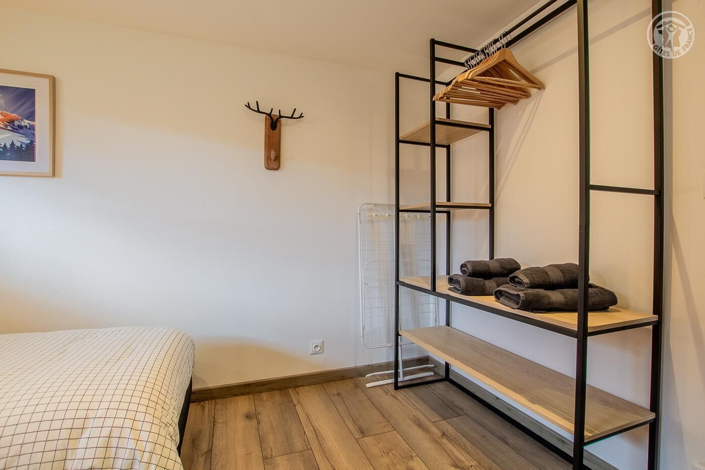 Ein Schlafzimmer mit einem Bett, einem hölzernen Kopfteil, einem Heizkörper, einem Regal mit gefalteten Handtüchern und einem an der Wand befestigten Hirschkopf.