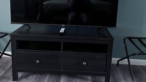 A flat-screen TV on a black entertainment center with two drawers, set against a blue wall with two abstract paintings.