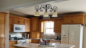 A kitchen with wooden cabinets, a central island with stools, a microwave, stove, refrigerator, and a trash can.