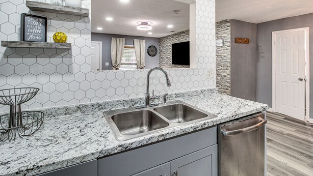A kitchen with a granite countertop, stainless steel sink, and a dishwasher. There are shelves with decorative items and a mirror above the sink. - Inviting Savannah Home w/ Yard: 3 Mi to Downtown! (Savannah)