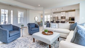 A spacious living room with a large sofa, two armchairs, and a coffee table. There is a dining area with a table and chairs in the background.