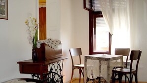 Een eethoek met een tafel voor vier personen, omringd door stoelen, een vaas met bloemen en een naaimachine.