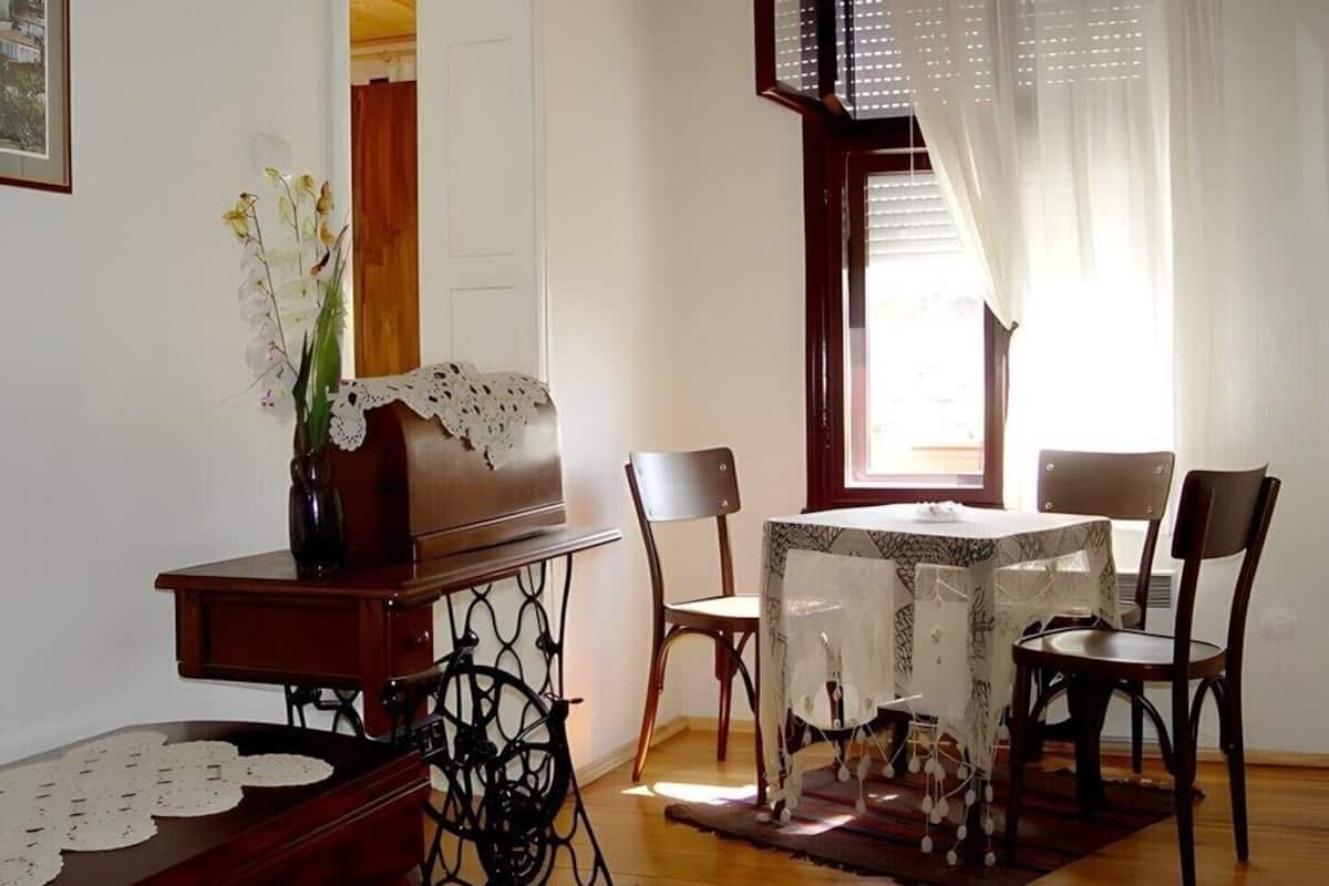 A dining area with a table set for four, surrounded by chairs, a vase with flowers, and a sewing machine.