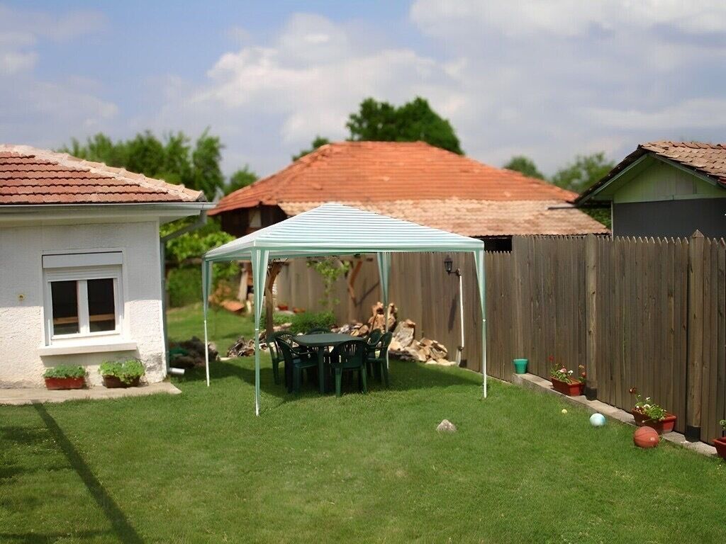 Ein Garten mit einem kleinen Patio-Tisch und -Stühlen unter einer weißen Markise, umgeben von einem Holzzaun und Topfpflanzen.