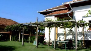 Een wit gebouw met een pannendak en een pergola begroeid met klimplanten.