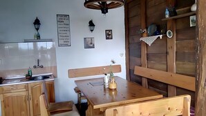 Een rustieke keuken met houten kasten, een houten eettafel met banken en een wandplank met keukengerei.