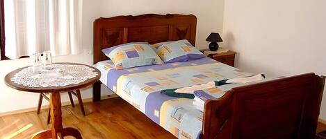 A bedroom with a wooden bed, a bedside table with a lamp, and a small round table with a lace tablecloth.