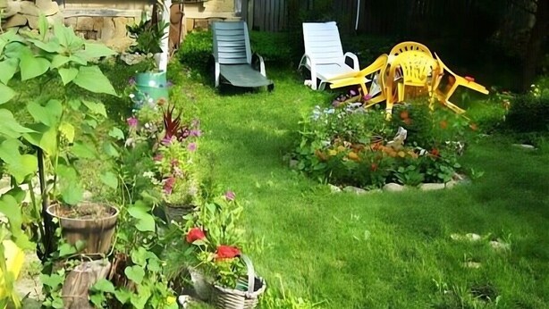 Een tuin met verschillende planten in potten en enkele buitenstoelen.